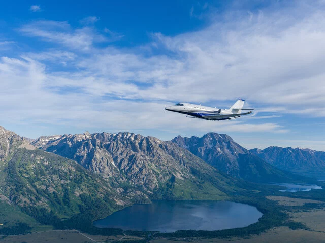 A Cessna Citation Latitude soaring over mountains.
