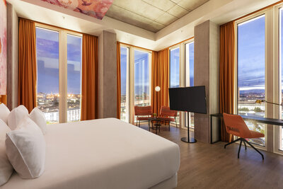 nhow_Frankfurt_Room_suite_curtains_open_king_size_bed_office_chair_armchairs_table_flower_lamps_tv_01-7360x4912