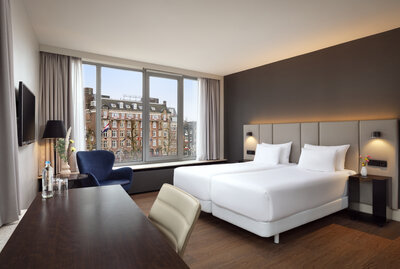 NH_Amsterdam_Caransa_Rooms_Superior_View_Twin_Bed_Daytime_Curtains_Open_TV_Flowers_Desk_Lounge_Chair_Bedside_Lights_On