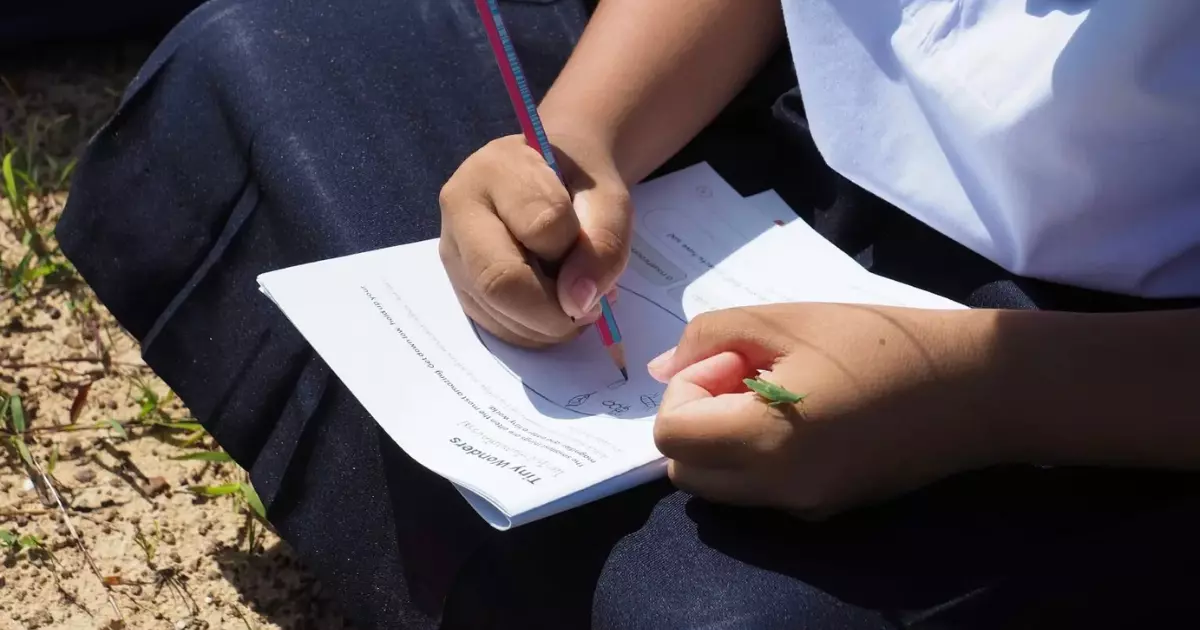 A student writes while a grasshopper sits on their hand
